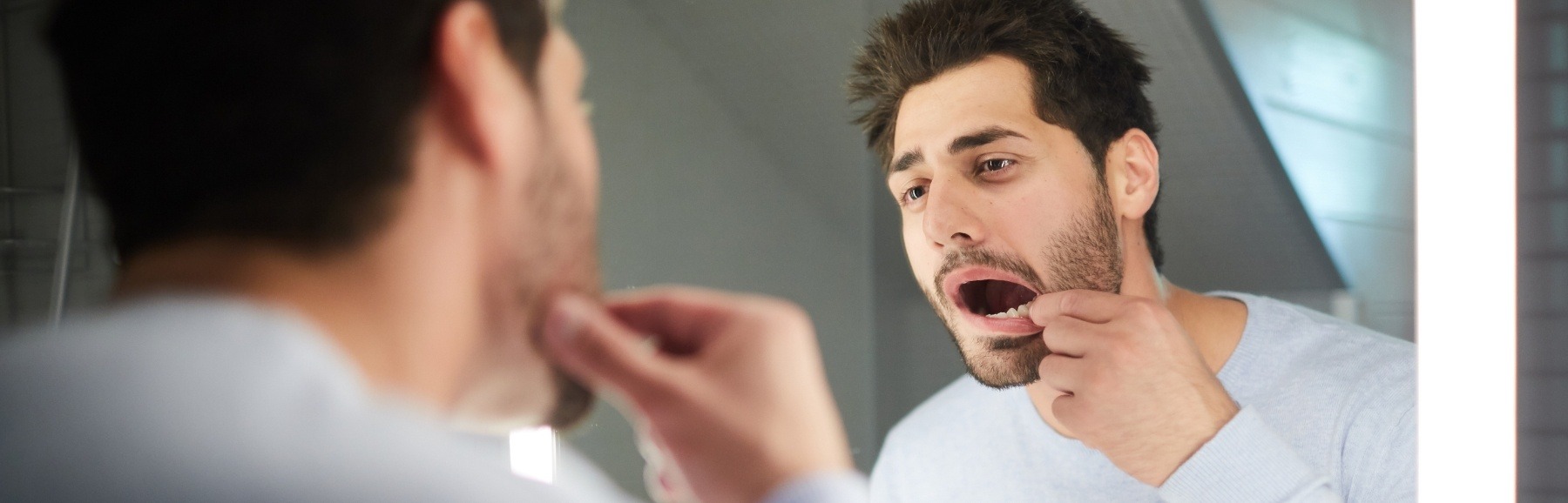 Man in need of emergency dentistry looking at his smile in the mirror
