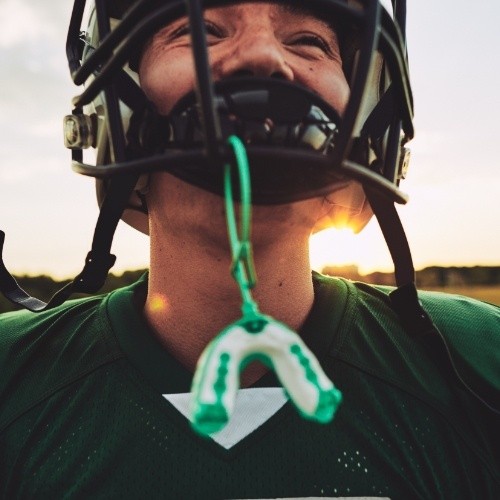 Teen with athletic mouthguard hanging from football helmet