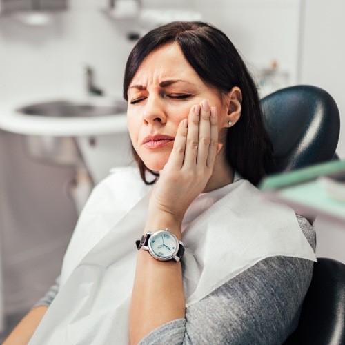 Woman holding cheek during emergency dentistry visit