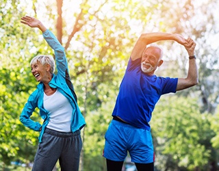 Senior couple with dental implant replacement teeth stretching in exercise clothes