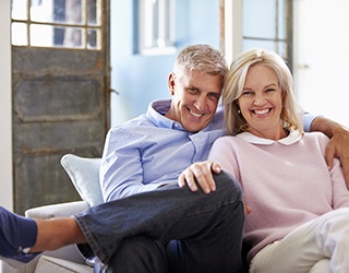 Man and woman sitting on a couch smiling after dental implant tooth replacement